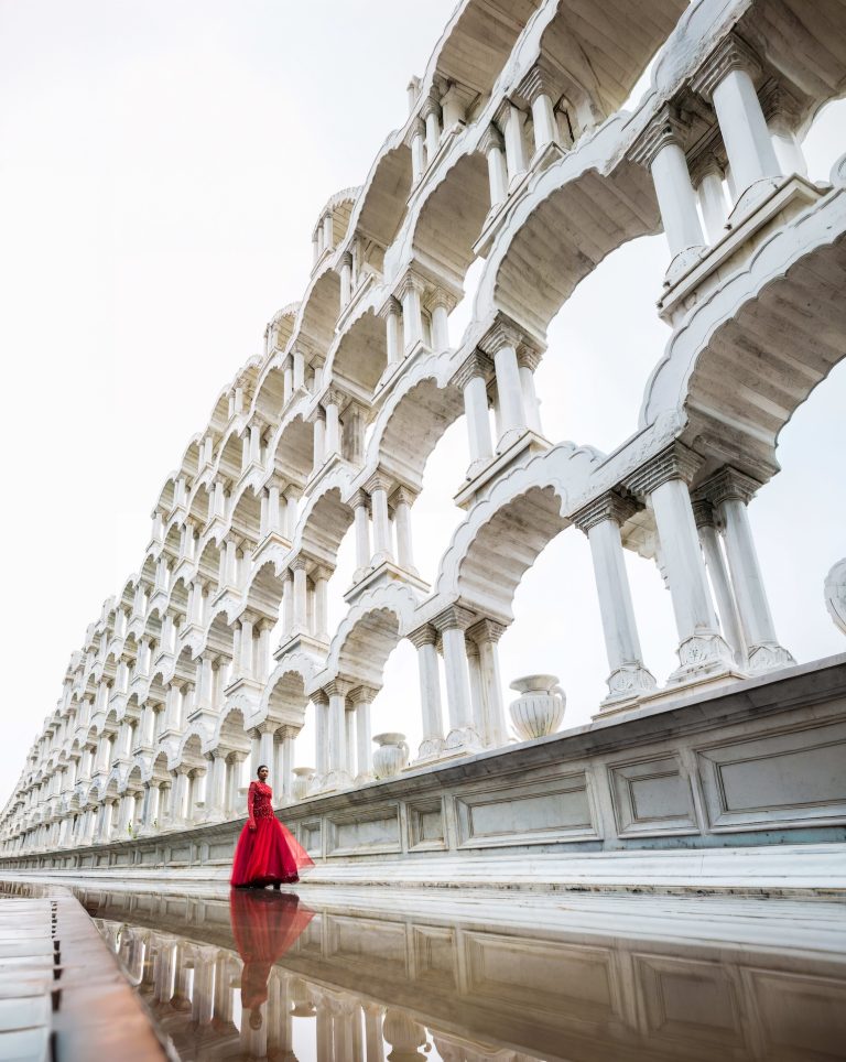 Model in a red gown beneath white arches in Jaipur, India, photographed by Indirect Media